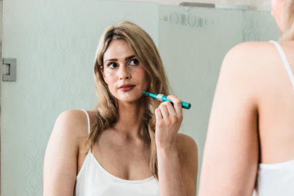 a lady looking at a mirror holding dr. pen a6s microneedling pen